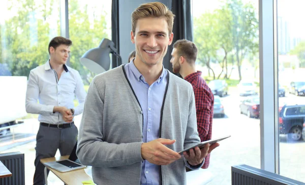 Χαμογελαστός νεαρός άνδρας χρησιμοποιώντας ψηφιακή δισκίο στο γραφείο. — Φωτογραφία Αρχείου