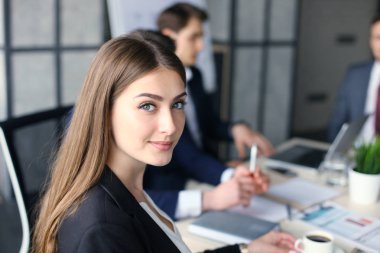 Çalışanlarıyla birlikte çalışan bir iş kadını, modern aydınlık ofiste arka planda çalışan insanlar..