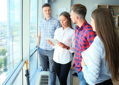 Group of young modern people in smart casual wear having a brainstorm meeting while standing in the creative office. clipart