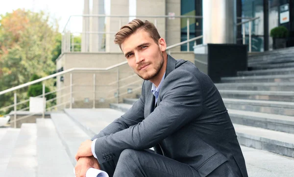 Hombre guapo ejecutivo de negocios sentado en las escaleras fuera de un edificio . — Foto de Stock