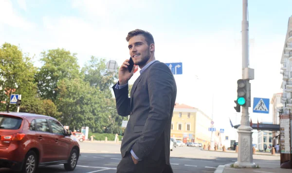 Joven hombre de negocios guapo cruzando la calle con teléfono móvil . — Foto de Stock
