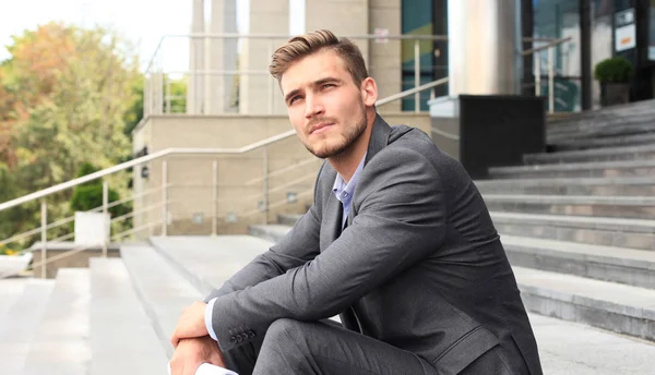 Hombre guapo ejecutivo de negocios sentado en las escaleras fuera de un edificio . — Foto de Stock