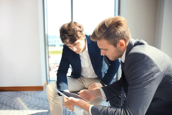 Rijpe zakenman met behulp van een digitaal tablet te bespreken van informatie met een jongere collega in een modern kantoor. — Stockfoto