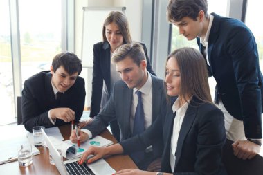 Girişim ekibi, modern parlak ofis içinde toplantı ve dizüstü bilgisayar üzerine çalışıyor.