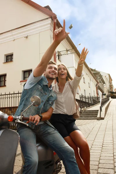 Feliz joven pareja montando scooter en la ciudad. Un chico guapo y una joven viajan. Concepto aventura y vacaciones . — Foto de Stock