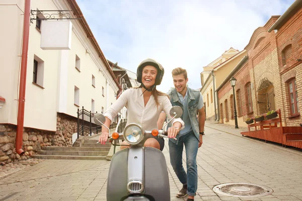 Feliz joven pareja montando scooter en la ciudad. Un chico guapo y una joven viajan. Concepto aventura y vacaciones . — Foto de Stock