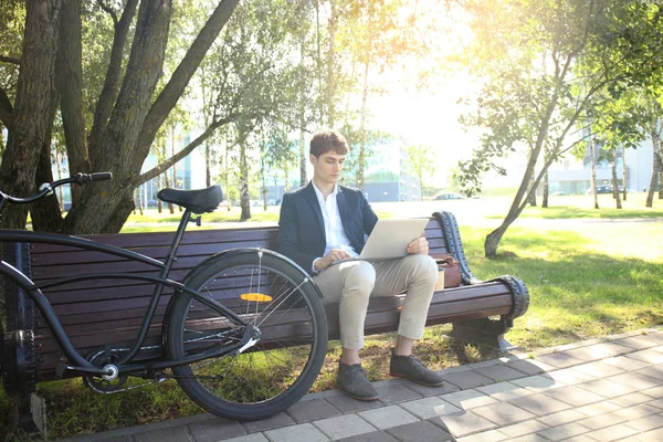 コーヒー ブレークの実業家。彼はベンチに座って、ノート パソコン、自転車の横で働く. — ストック写真