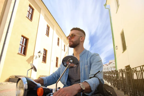Neşeli genç adam şehirde scooter üzerinde biniyor.