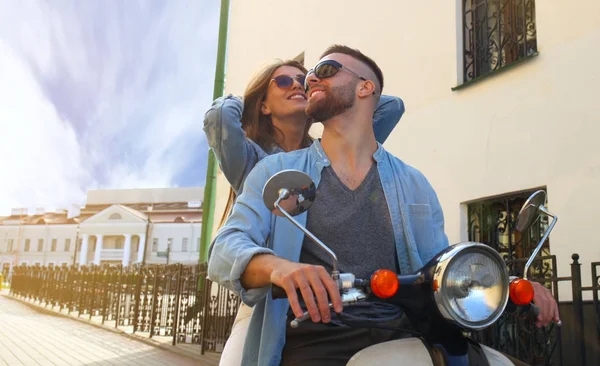 Feliz joven pareja montando scooter en la ciudad. Un chico guapo y una joven viajan. Concepto aventura y vacaciones . — Foto de Stock