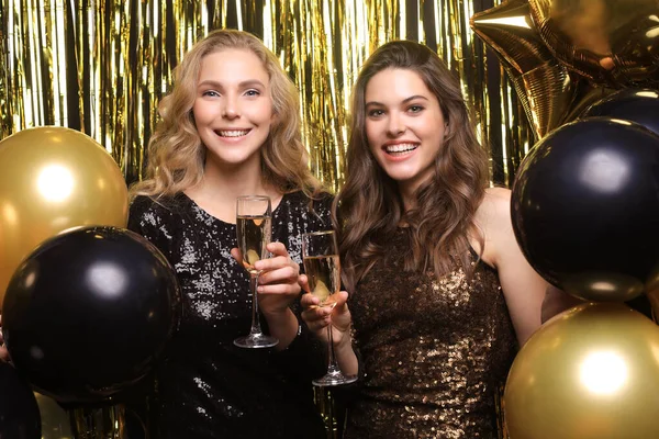Due signorine che bevono champagne. Immagine di ragazze con palloncini isolati su sfondo oro . — Foto Stock