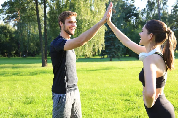 Feliz jovem casal dando alta cinco enquanto de pé no parque . — Fotografia de Stock