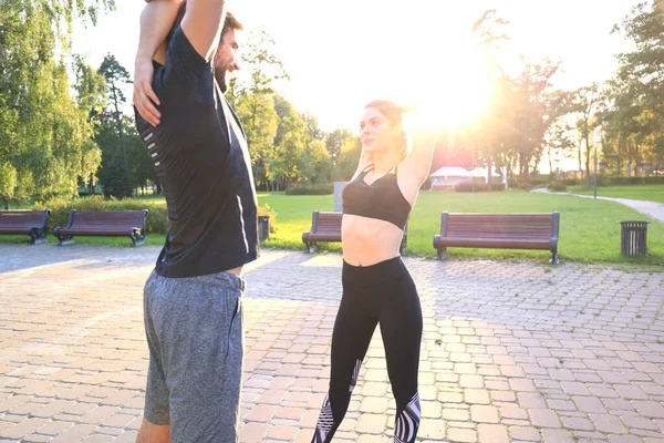 Attractive couple doing stretch together and smiling while working out in park outdoors. — Stock Photo, Image