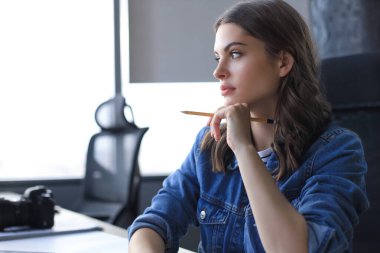 Yoğunlaşmış genç bir kadın ofiste çalışırken bir şeyler yazıyor..