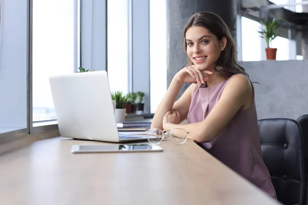 Piękna uśmiechnięta bizneswoman siedzi w biurze i patrzy w kamerę — Zdjęcie stockowe