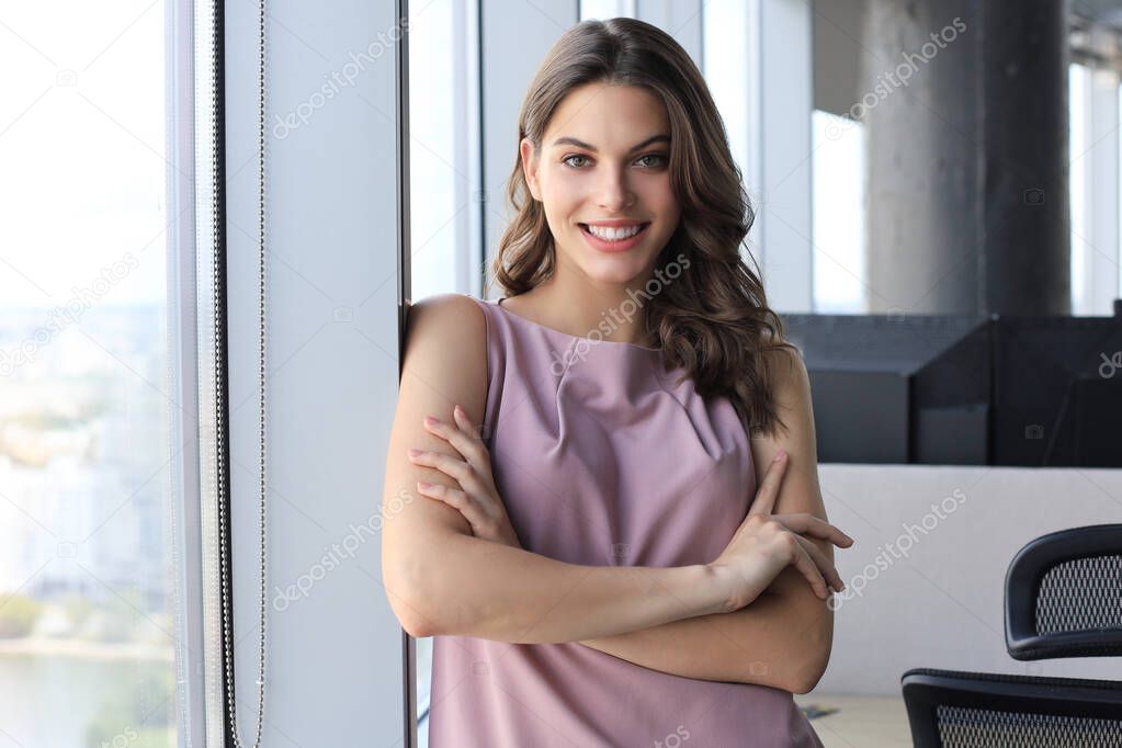 Attractive business woman looking at camera and smiling while standing in the office near the window