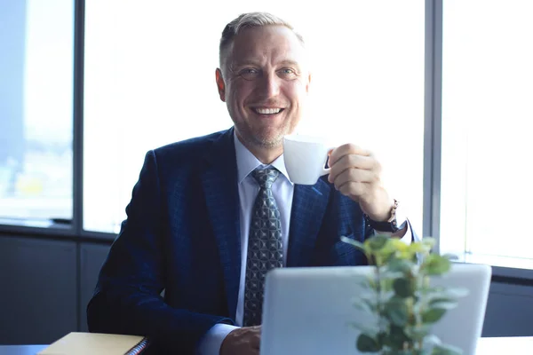 Volwassen zakenman werkt op computer en koffie drinken in modern kantoor. — Stockfoto