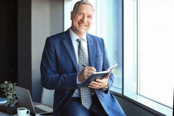 Empresario de mediana edad trabajando y tomando notas en su moderna oficina . — Foto de Stock