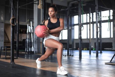 Formda ve kaslı bir kadın spor salonunda ilaç topuyla egzersiz yapıyor..
