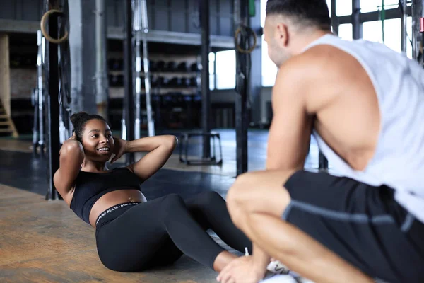 Entrenador ayudando a las jóvenes a hacer ejercicios abdominales en el gimnasio. — Foto de Stock