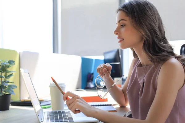 Mulher bonita usando laptop e olhando para ele enquanto sentado em seu local de trabalho . — Fotografia de Stock