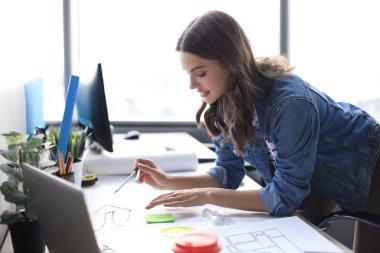 Taslak üzerinde pusula olan genç mimar çizimi ve yaratıcı ofiste çalışırken gülümsemesi..