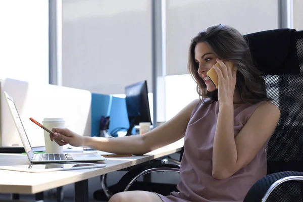オフィスのデスクに座っている間、携帯電話で同僚と話す魅力的なビジネス女性 — ストック写真