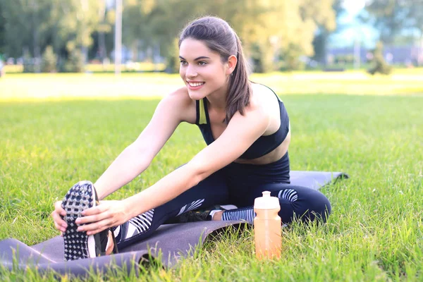 Jovem mulher fitness atraente se exercitando ao ar livre, exercícios de alongamento . — Fotografia de Stock