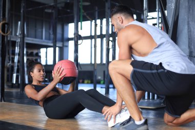 Spor salonunda genç bir bayana karın egzersizi yaptıran antrenör..