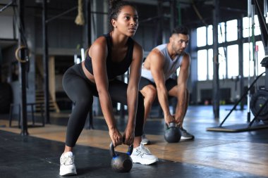 Formda ve kaslı bir çift spor salonunda egzersiz yaparken dambıl kaldırmaya odaklanmış..