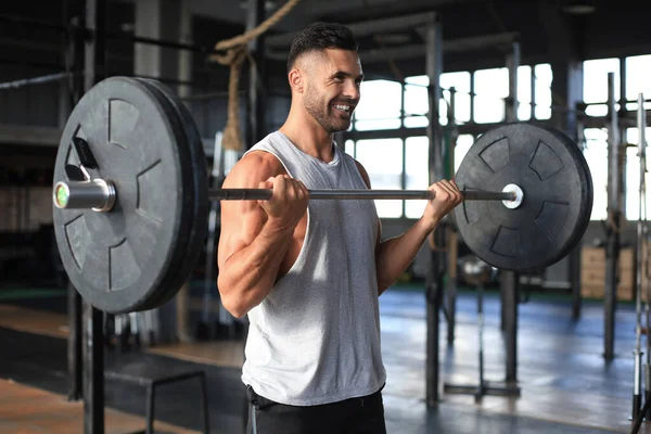 Homem musculoso trabalhando no ginásio fazendo exercícios com barra no bíceps . — Fotografia de Stock