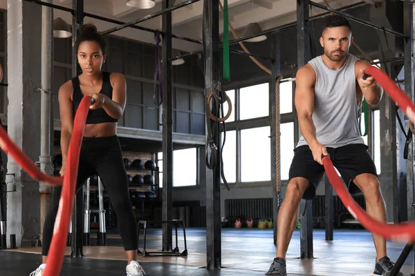 Pareja joven atlética con cuerda de batalla haciendo ejercicio en gimnasio de fitness de entrenamiento funcional. — Foto de Stock