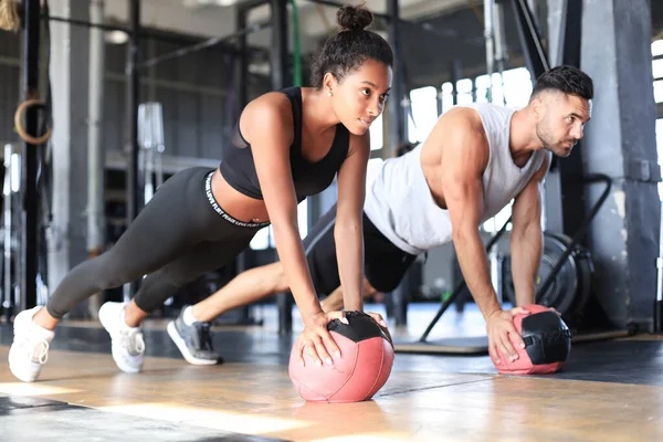 Hermosa pareja de jóvenes deportes está trabajando con la pelota de la medicina en el gimnasio. — Foto de Stock