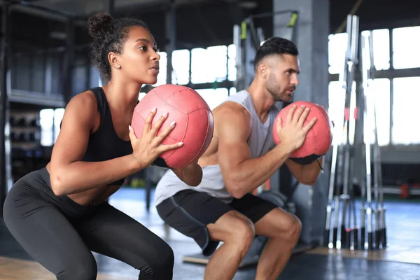 Hermosa pareja de jóvenes deportes está trabajando con la pelota de la medicina en el gimnasio. — Foto de Stock