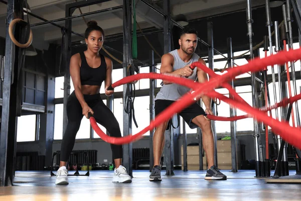Atlético jovem casal com corda de batalha fazendo exercício no ginásio de fitness de treinamento funcional. — Fotografia de Stock