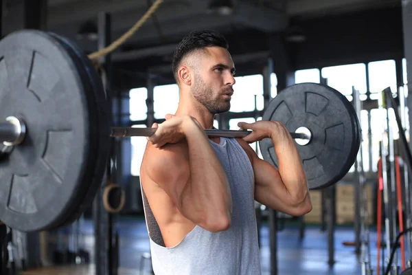 Homem musculoso trabalhando no ginásio fazendo exercícios com barra no bíceps . — Fotografia de Stock