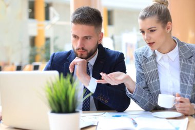 Başlangıç projesinde işbirliği yaparken ofiste dizüstü bilgisayar kullanan iki genç iş adamı.