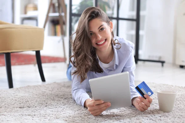 Morena natural feliz con tarjeta de crédito y tableta digital en la sala de estar . —  Fotos de Stock