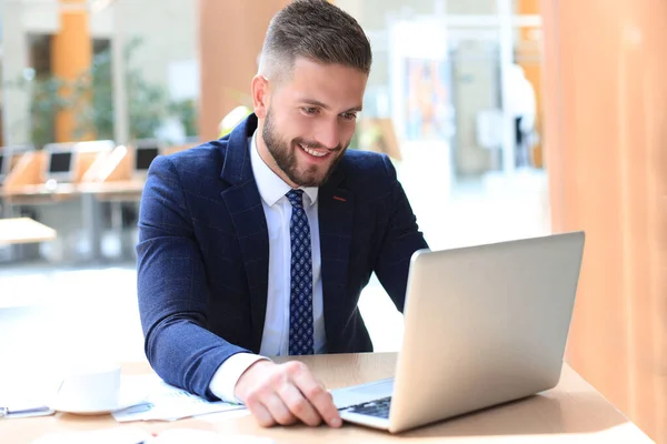 Uomo sorridente seduto in ufficio e utilizzando il suo computer portatile . — Foto Stock