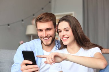 Genç çift evdeki kanepede oturmuş akıllı bir telefonla online içeriği izliyorlar..