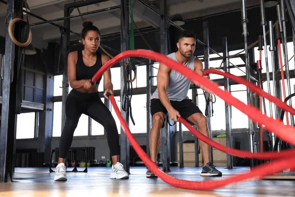 Athletic young couple with battle rope doing exercise in functional training fitness gym.