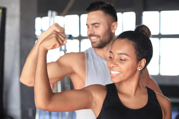 Alegre pareja deportiva entrenando juntos y mostrando bíceps en el gimnasio . — Foto de Stock