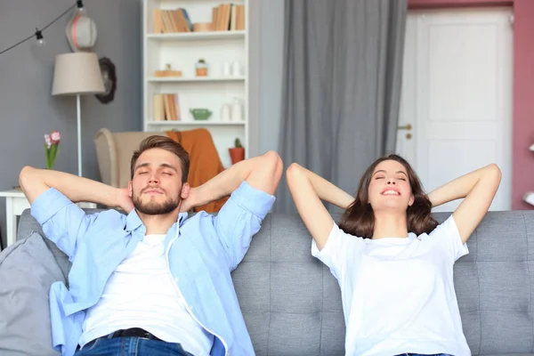 Sonriendo hermosa pareja sentada en un sofá y soñando con un nuevo hogar. —  Fotos de Stock