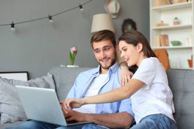 Genç çift evde bazı online alışveriş yapıyor, kanepede bir dizüstü bilgisayar kullanarak.
