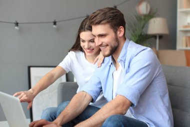 Genç çift evde bazı online alışveriş yapıyor, kanepede bir dizüstü bilgisayar kullanarak.