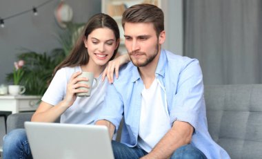 Genç çift evde bazı online alışveriş yapıyor, kanepede bir dizüstü bilgisayar kullanarak.