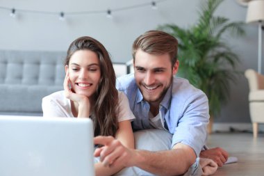 Genç çift evde bazı online alışveriş yapıyor, katta bir laptop kullanarak.