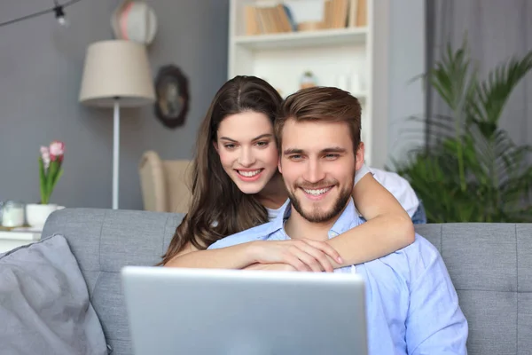 Pareja joven haciendo algunas compras en línea en casa, utilizando un ordenador portátil en el sofá . —  Fotos de Stock