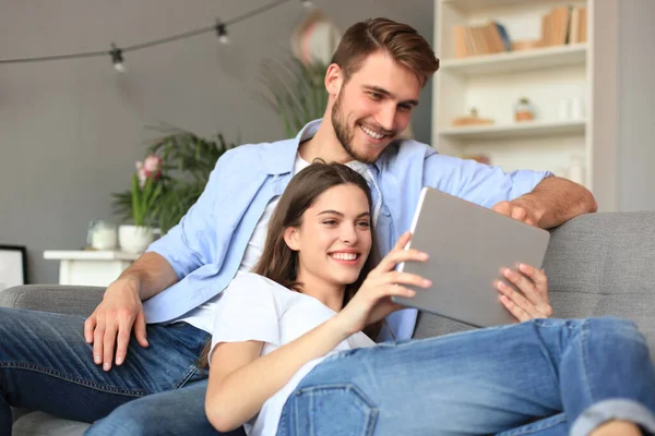 Jong stel kijken media-inhoud online in een tablet zitten op een bank in de woonkamer. — Stockfoto
