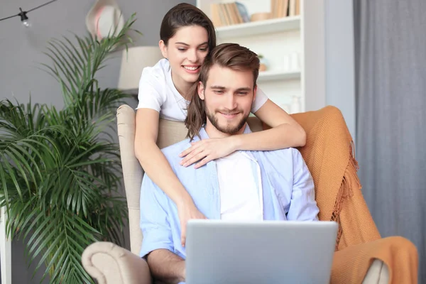 Casal jovem fazendo algumas compras on-line em casa, usando um laptop no sofá . — Fotografia de Stock