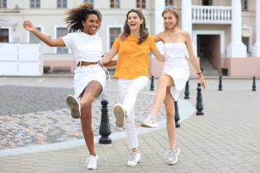 Sokakta poz veren üç genç, gülümseyen hippi kadın. Olumlu yüz ifadeleri sergiliyor. Dans etmek..